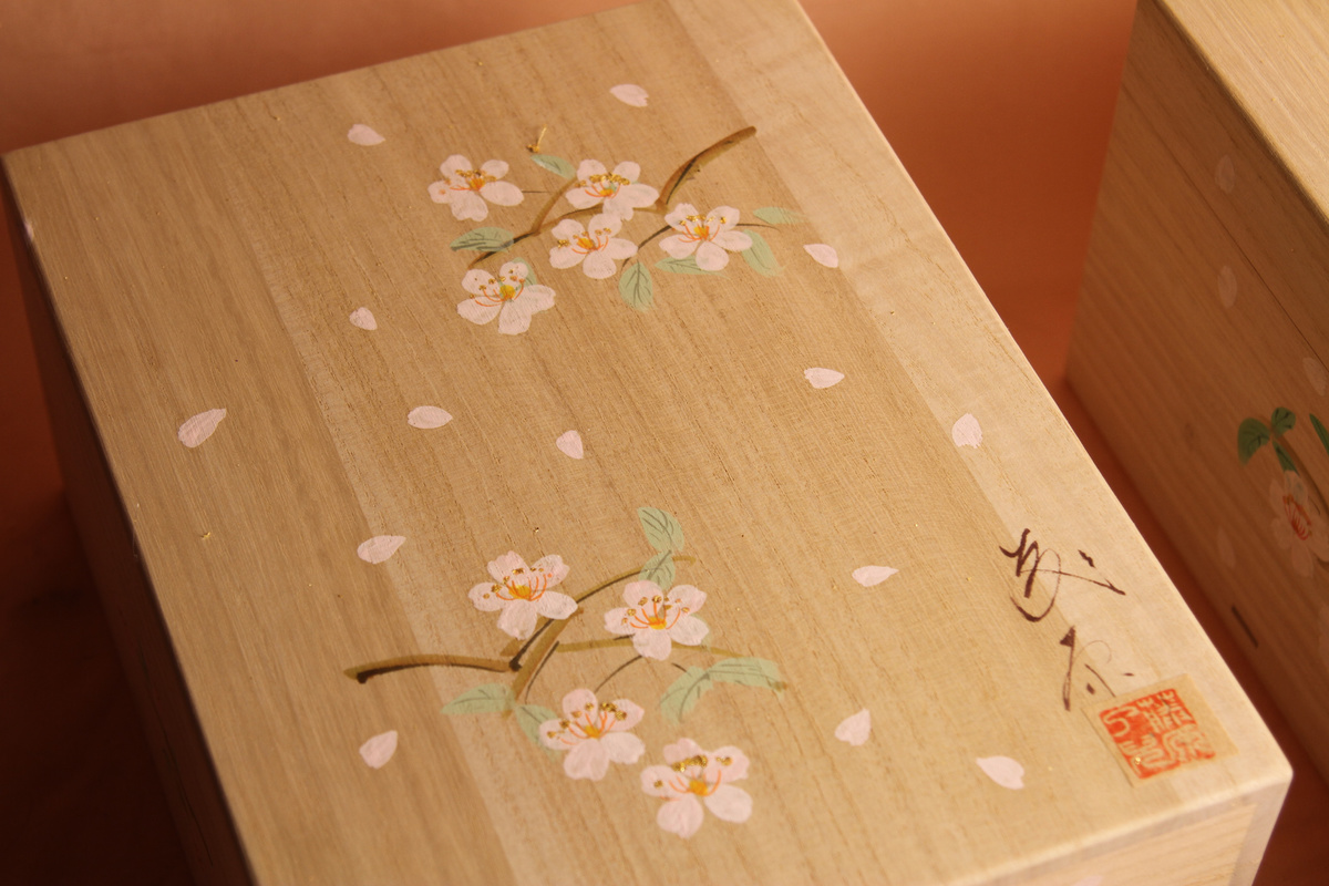みかわ工房特別制作の桐箱で、桐箱の四方に手描きで桜の花びらを一つ一つ描いています。また、末永い保存が効くように紐も平織りの綿地を使用しています。